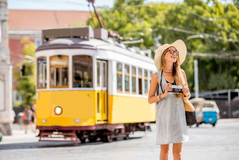 Chica tomando fotos en Alfama con una típica tranvía detrás de ella en el Tour a Lisboa, Portugal